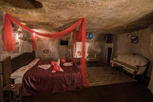 a bedroom with a bed in a cave with red curtains at Kapadokya Ihlara Konaklari & Caves in Guzelyurt