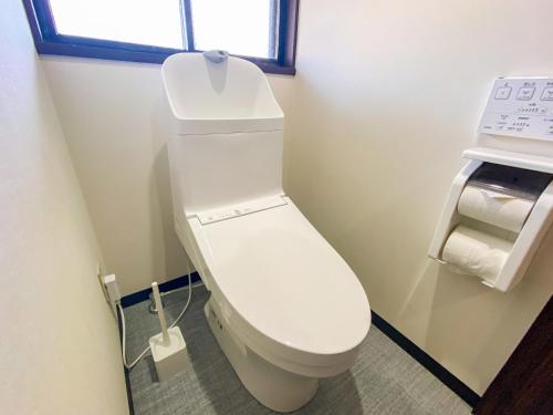 a white toilet in a bathroom with a window at 丘の上から海が見える一棟貸しヴィラ しまいろ長手 in Nagate