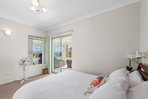 a white bedroom with a bed and a fan at Bayview Towers in Nelson Bay