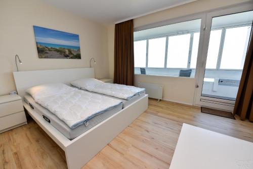 a white bedroom with a bed and windows at Haus "Atlantic" Appartement ATL 604B in Cuxhaven