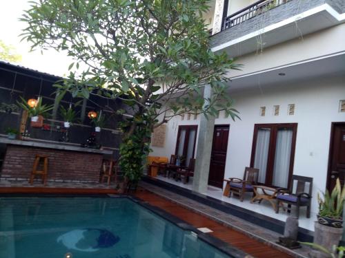a swimming pool in front of a building with a tree at Pujihouse One in Legian