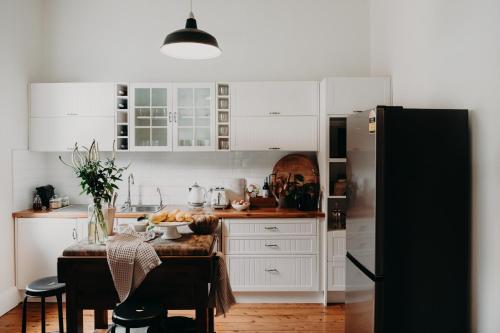 cocina con armarios blancos, mesa y nevera en The Pioneer - A Luxurious, Federation Home. en Dubbo