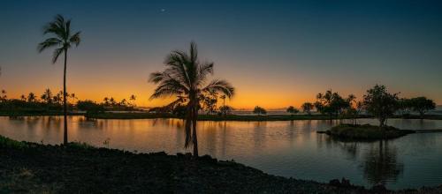 a sunset with palm trees and a body of water at Mauna Lani Terrace G102 - Lagoon View Terrace Suite - Upscale Luxury Waterfront in Waikoloa