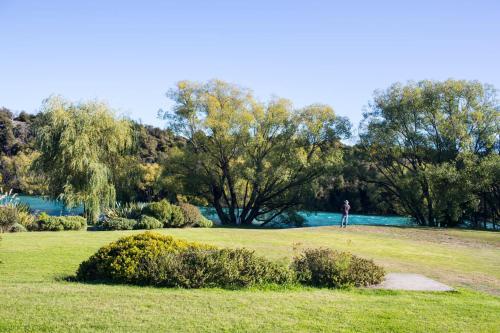 a person standing on a field with trees and water at The River House Wanaka in Wanaka