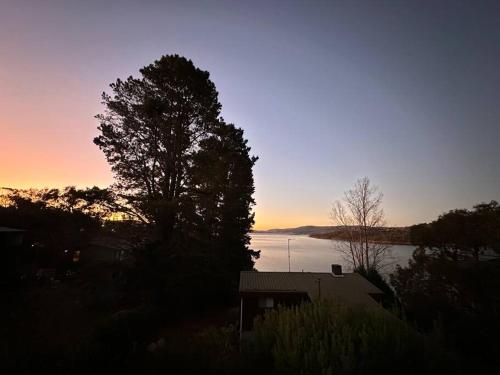 a sunset over a lake with a house and a tree at Jindabyne Lake View in Jindabyne