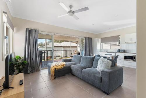 a living room with a gray couch and a kitchen at The Leaning Oak Holiday Lifestyles - Lake Conjola in Conjola