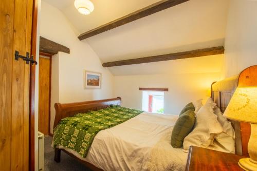 a bedroom with a bed with a green blanket on it at Maes Madog Cottages in Betws-y-coed