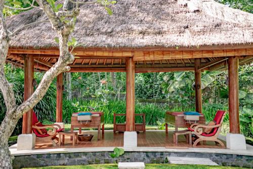 a pavilion with chairs and tables and a thatch roof at The Lotus Residence by Amerta Experience in Tabanan