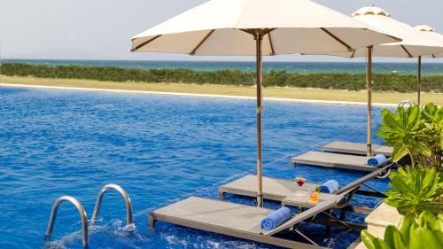 a pool with chairs and umbrellas and the ocean at Wyndham Garden Cam Ranh Resort in Cam Ranh