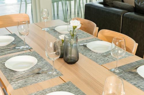 a wooden table with white plates and wine glasses at The Stay Huahin - Luxury Private Pool Villa in Khao Tao