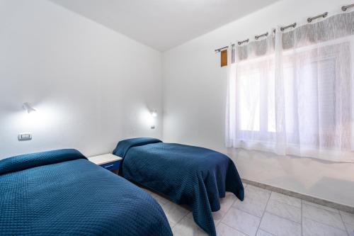 two beds in a bedroom with blue sheets and a window at B&B il Rifugio in Carbonia