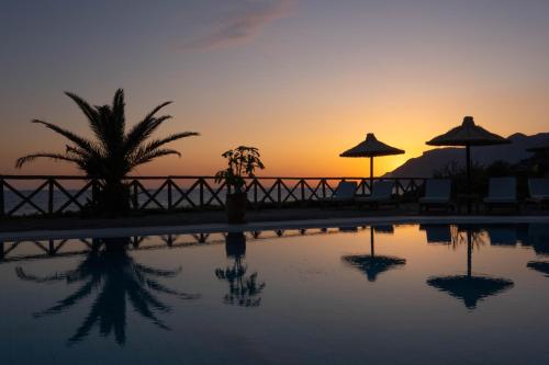 a sunset over a pool with chairs and umbrellas at Mochlos Blue in Mochlos