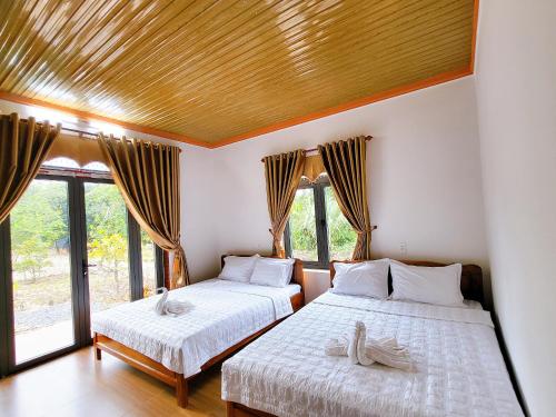 two beds in a room with windows and a wooden ceiling at Cat Tien Farmer Lodge in Quan Tom