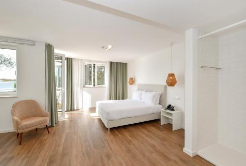 a white bedroom with a bed and a chair at Serpa Hotel in Serpa