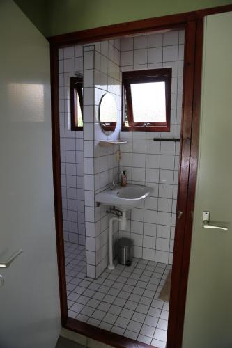a white tiled bathroom with a sink and a mirror at Huisje Vogelsand in 't Horntje