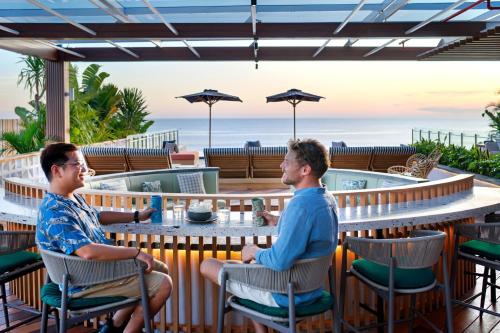 two men sitting at a table with the ocean in the background at Tribe Bali Kuta Beach in Kuta