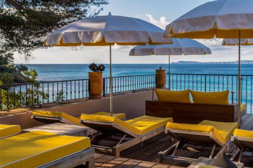 a group of chairs and umbrellas on a deck with the ocean at Hôtel Le Bailli De Suffren in Rayol-Canadel-sur-Mer