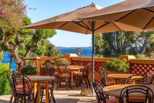 a patio with tables and chairs and an umbrella at Les Terrasses du Bailli in Rayol-Canadel-sur-Mer
