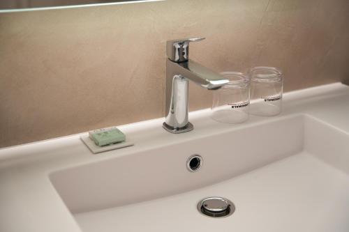 ein Waschbecken mit einem Wasserhahn und zwei Gläsern darauf in der Unterkunft Hôtel du Golf de l'Ailette, The Originals Relais (Qualys-Hotel) in Chamouille