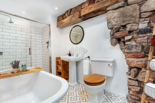 a bathroom with a white tub and a stone wall at Honeybee Cottage- stunning home on Fife coast in Anstruther