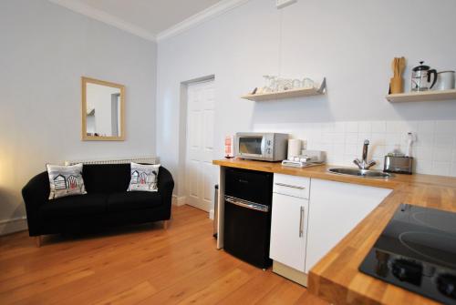 a kitchen with a black couch and a microwave at Market Apartment- harbourfront studio Pittenweem in Pittenweem