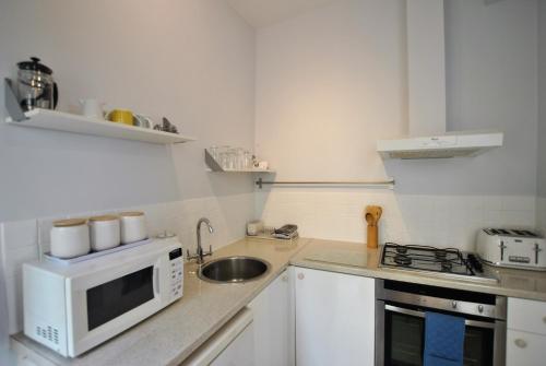 a white kitchen with a sink and a microwave at Gyles Apartment - harbourfront studio Pittenweem in Pittenweem