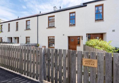 a house with a wooden fence with a sign on it at Coastal Haven- stunning home in Crail in Crail
