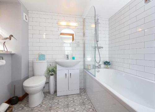 a white bathroom with a toilet and a tub and a sink at East Pier View- stunning shorefront home in Saint Monance