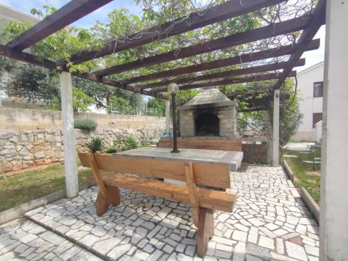 a wooden bench sitting under a pergola with a fireplace at Apartment Alafetic in Krk