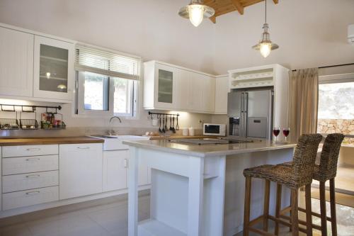 a kitchen with white cabinets and a island with bar stools at Villa Asteri, Old Skala - Secluded Location - Panoramic Sea Views - Infinity Pool in Old Skala