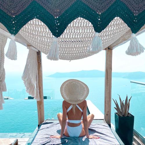 a woman in a bikini and a hat sitting on a beach at Galaxy Suites & Villas in Imerovigli