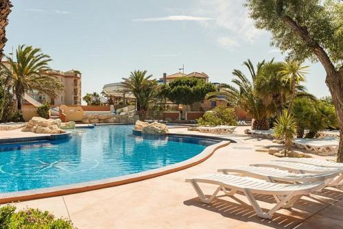 a swimming pool with two lounge chairs and palm trees at Mobil Home Camping Mar Estang 4* in Canet-en-Roussillon
