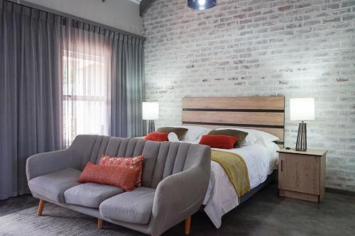 a bedroom with a bed and a couch and a brick wall at The Featherbed - Oudtshoorn in Oudtshoorn