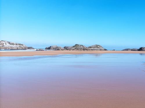 una playa con agua rosa y rocas de fondo en Camping Playa de Ris, en Noja