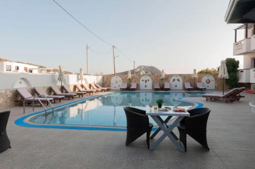 einen Pool mit einem Tisch und Stühlen neben einem Gebäude in der Unterkunft Arkasa Bay Hotel in Arkasa