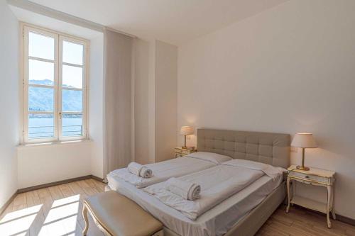a large bed in a white bedroom with two windows at Maioliche Apartments Griante in Griante Cadenabbia