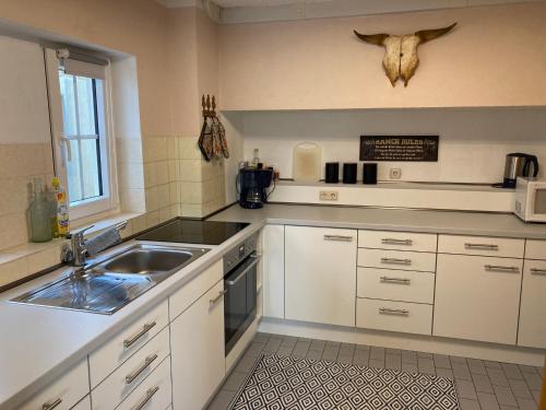 een keuken met witte kasten en een wastafel en een schedel aan de muur bij Haus Vaquero - Rancho el Rosal in Bad Mergentheim