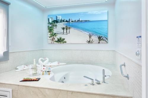 Hospedium Hotel Abril في سان خوان دي أليكانتي: حوض استحمام في حمام مع لوحة على الشاطئ