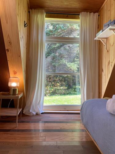 a bedroom with a large window with white curtains at Au Sommet du Fjord in Sacré-Coeur-Saguenay