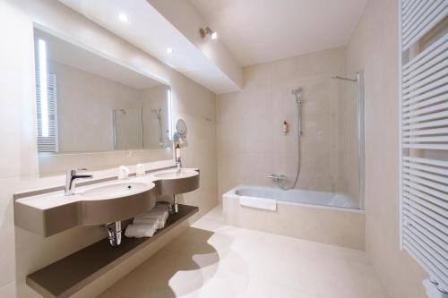 a bathroom with a sink and a tub and a mirror at Hotel Les Jardins De La Molignée in Dinant