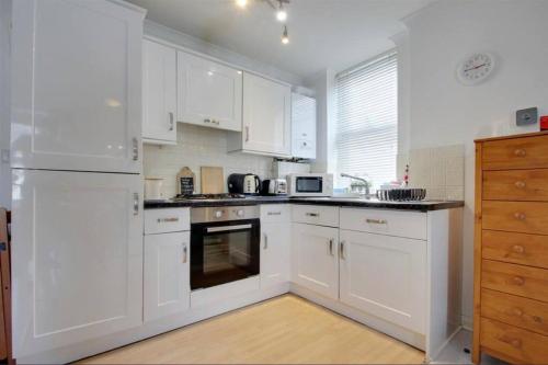 una cocina blanca con armarios y electrodomésticos blancos en Stunning seaside studio en Worthing