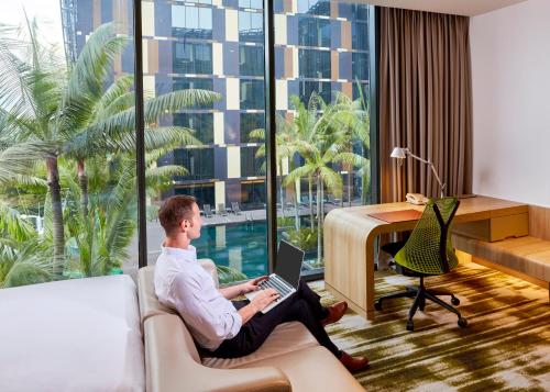 a man sitting on a couch with a laptop in a hotel room at Crowne Plaza Changi Airport by IHG in Singapore