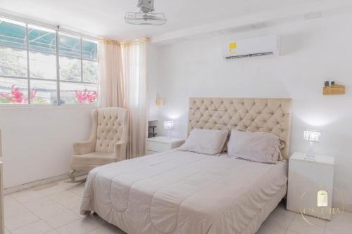a white bedroom with a large bed and a chair at Hostal Casa Dandy in Cartagena de Indias