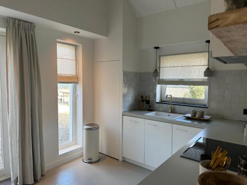 a kitchen with white cabinets and a sink and windows at Stijlvol huisje in de Brabantse natuur! Tuynloodz B in Beers