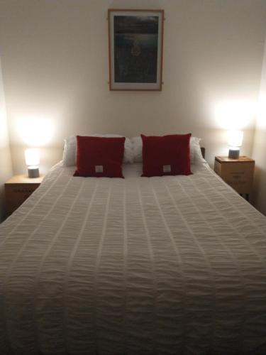 a white bed with two red pillows on it at Snowberry Cottage in Borve