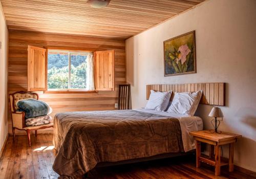 a bedroom with a bed and a chair and a window at Hotel e Pousada Montanha Real in Urubici