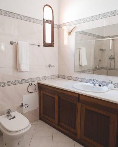 a bathroom with a sink and a toilet and a mirror at Casa das Palmeiras - Villa com piscina, BBQ e ar condicionado in Albufeira