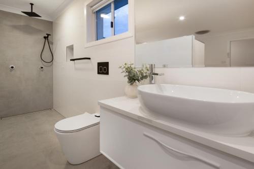 a white bathroom with a sink and a toilet at Beach Retreat in Sydney