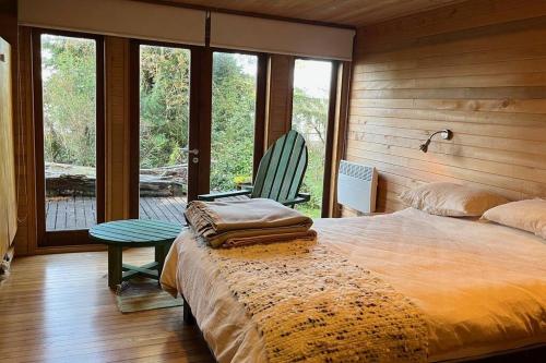 Schlafzimmer mit einem Bett, einem Stuhl und Fenstern in der Unterkunft Refugio Arquitectónico frente al Mar in Ancud