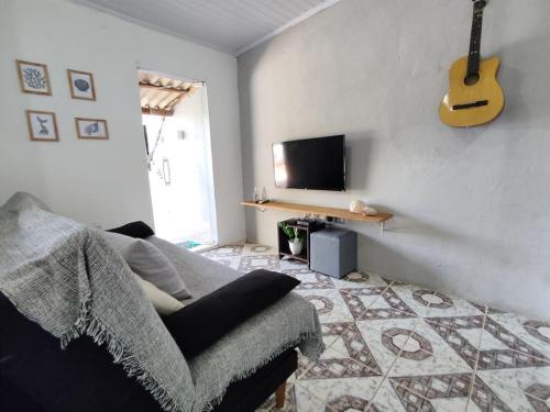 uma sala de estar com um sofá, uma televisão e uma guitarra em Lopes House Araçatiba em Praia de Araçatiba